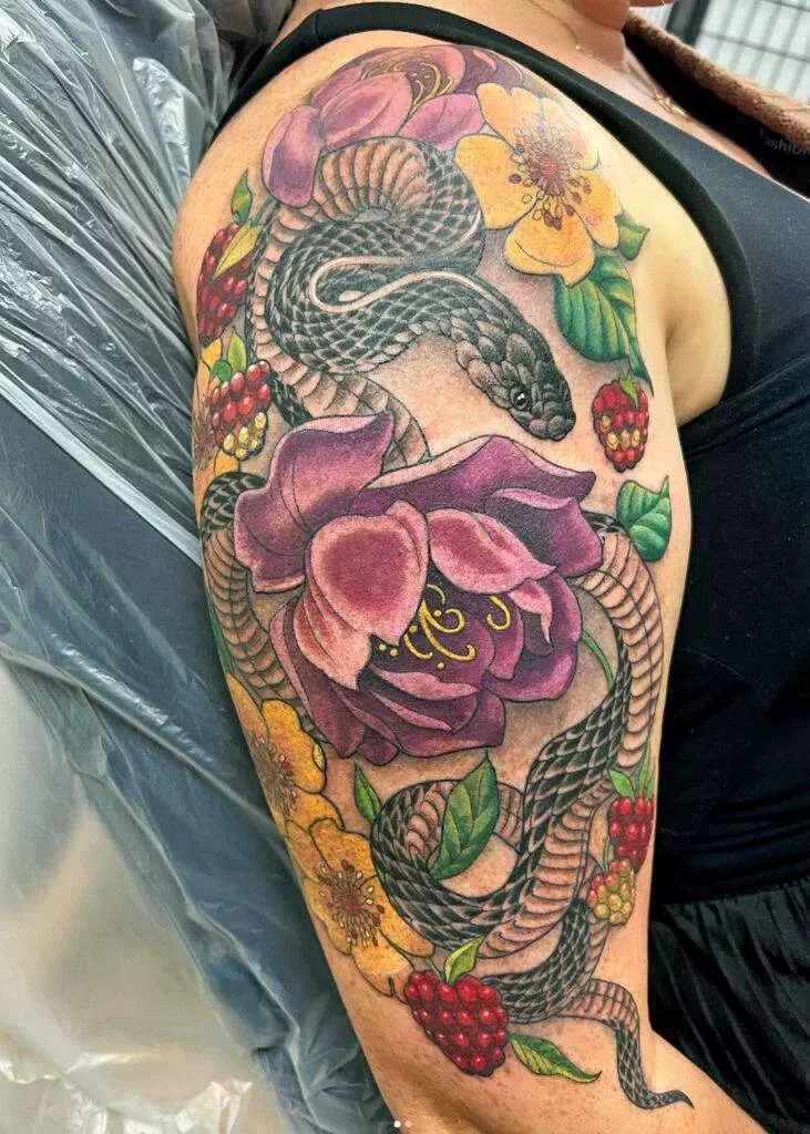 A colorful tattoo featuring a snake intertwined with large purple and yellow flowers and red berries on an upper arm.