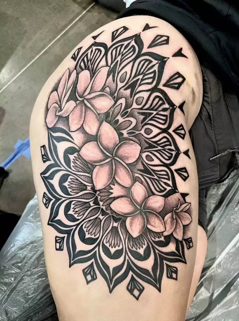 A thigh tattoo featuring intricate floral and geometric designs, combining black and shaded elements with prominent blooming flowers.